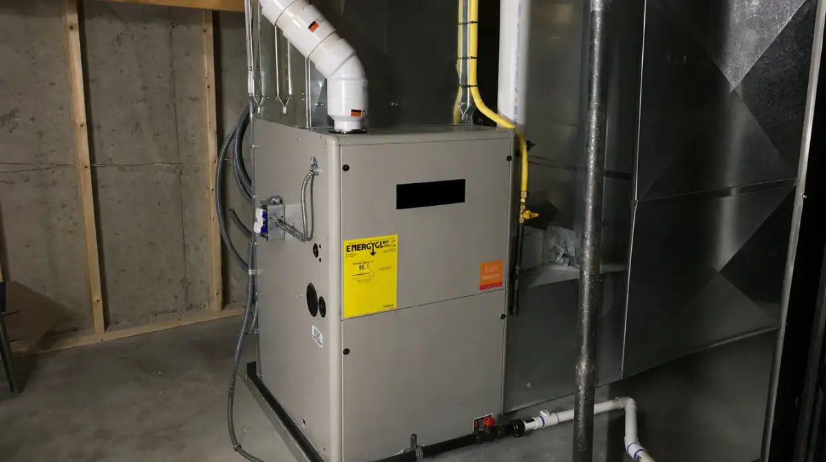 A newly installed high-efficiency gas furnace standing in an unfinished basement, with the flue and supply plenum connected above it