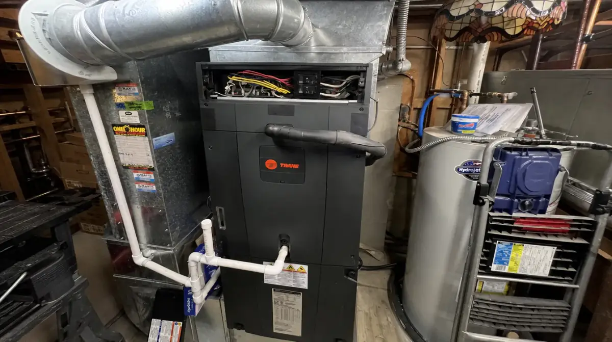 An older furnace and air handler surrounded by round duct trunks in a crowded basement