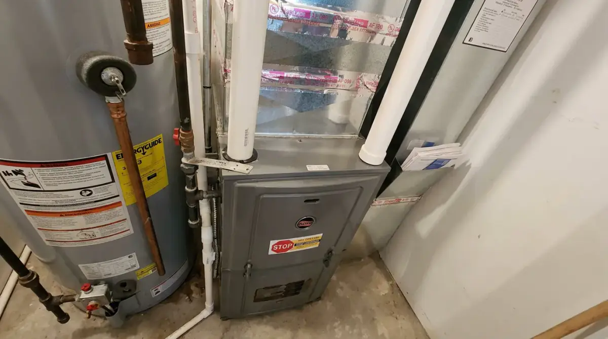 A propane furnace installed next to a gas water heater in a utility closet with the vent piping run overhead